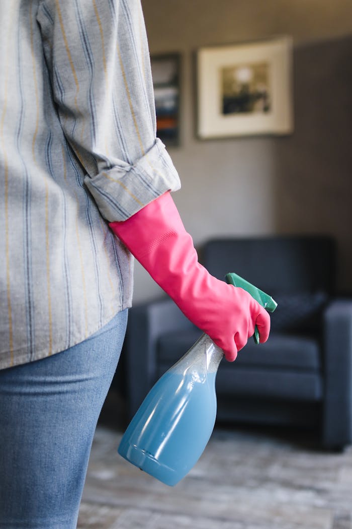 Close-up of a person in pink gloves holding a blue spray bottle indoors.