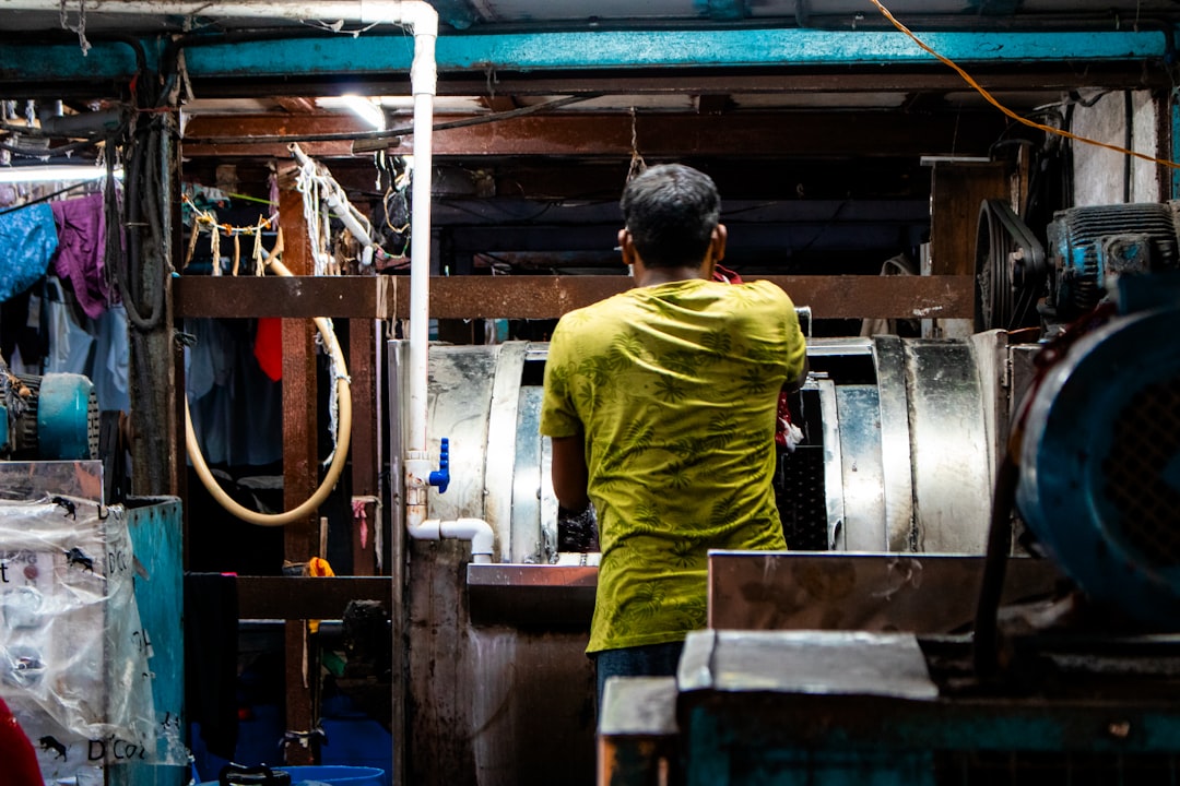 A worker loading clothes into an industrial washing drum inside Dhobi Ghat in Mumbai. It is suitable for use in articles, presentations, research on informal economies, and visual documentation of workplace environments in India.